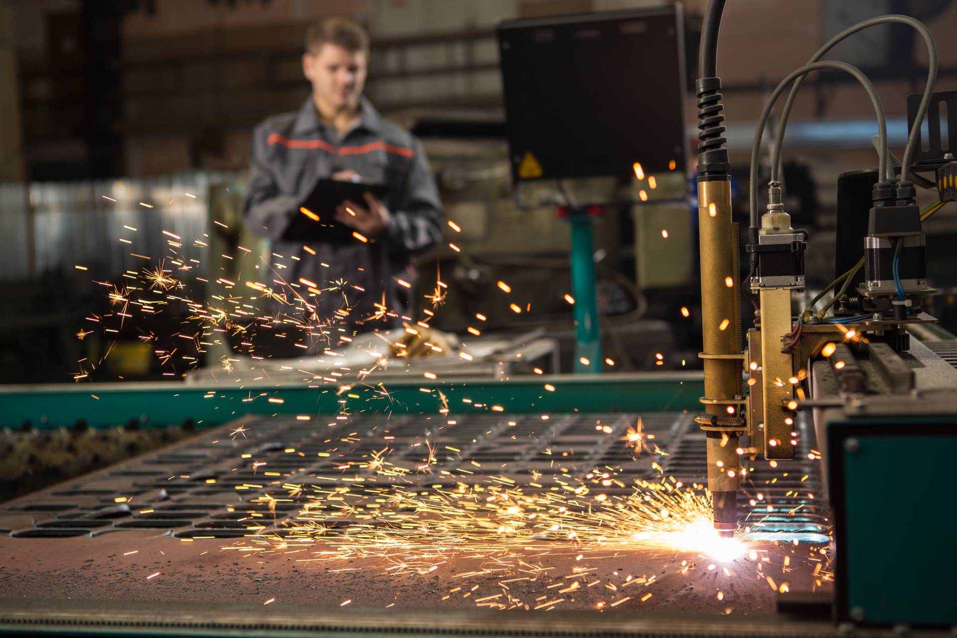 Photograph of a metal laser cutter and a workman in the background with a clipboard