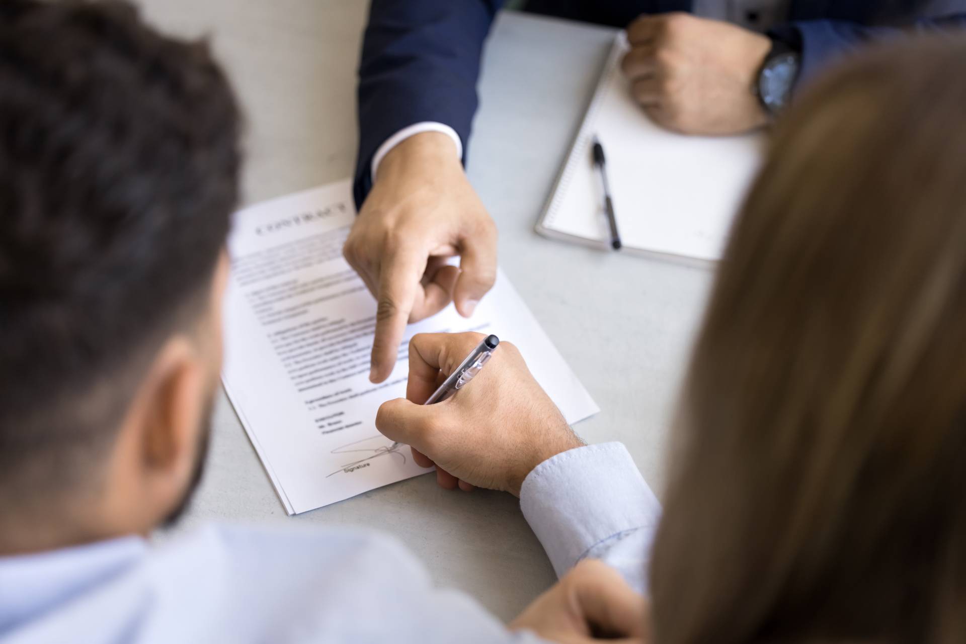 Photograph of a solicitor pointing two people towards where to sign on a formal, paper contract