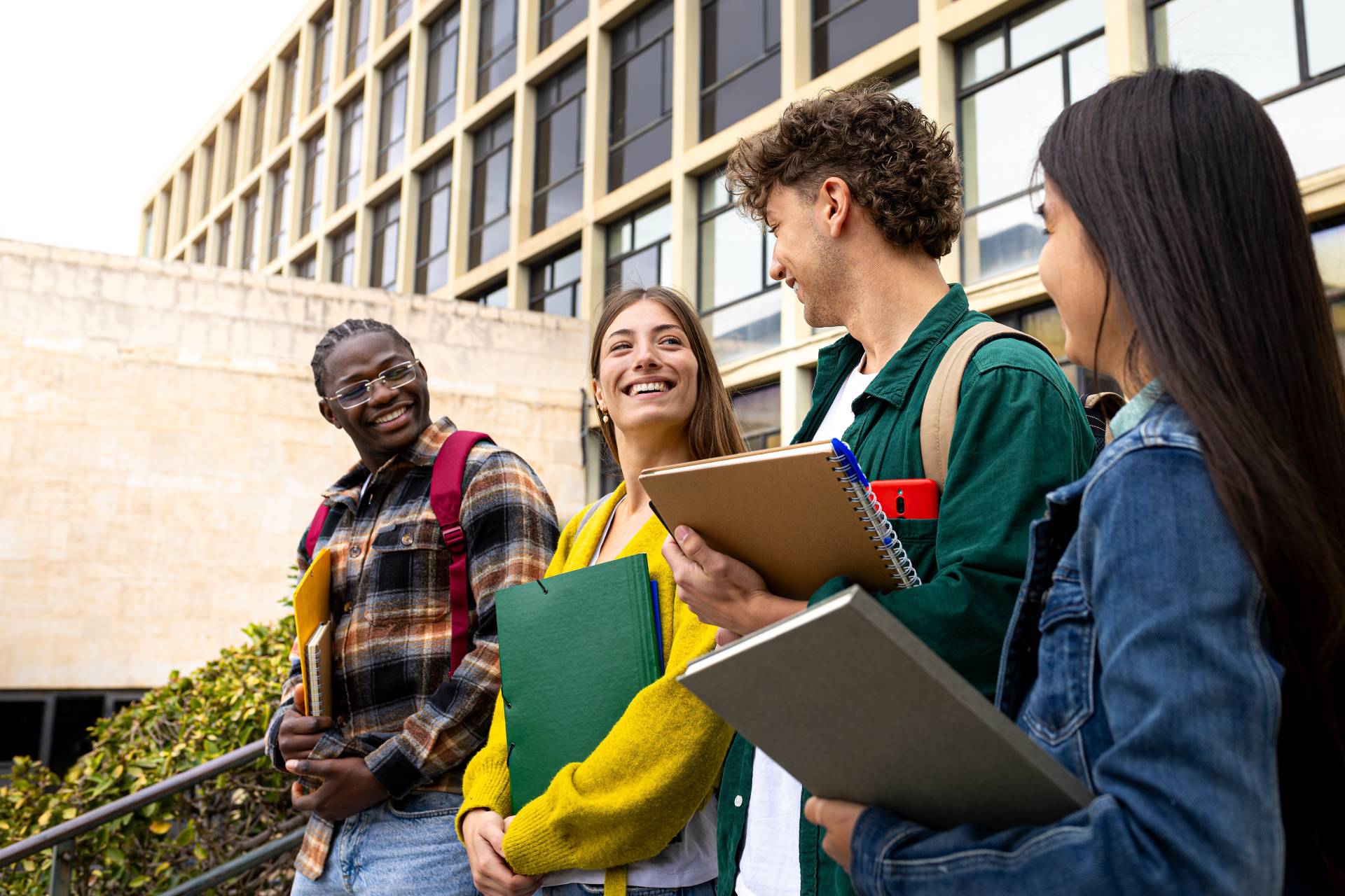 Photograph of four students, carrying folders and notebooks and smiling together