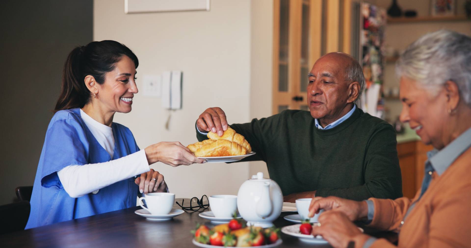 Photograph of a carer offering breakfast pastries to two older people