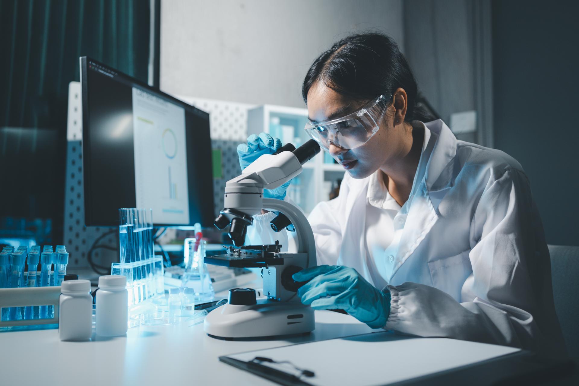 Photograph of a scientist looking into a microscope, surrounded by scientific equipment and a computer