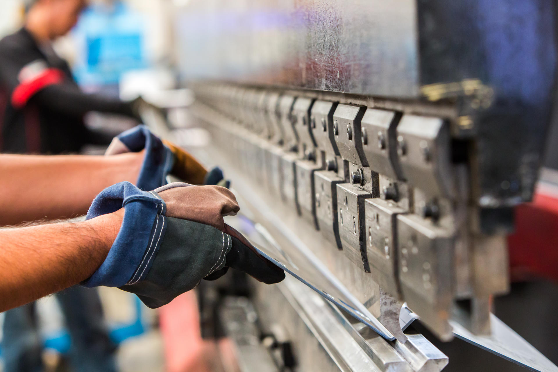 Photograph of workers putting a large metal sheet into a metal bending machine