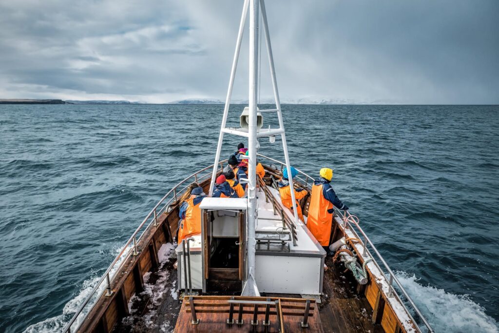 Photograph of a fishing boat, on the sea, with fishermen in orange jackets