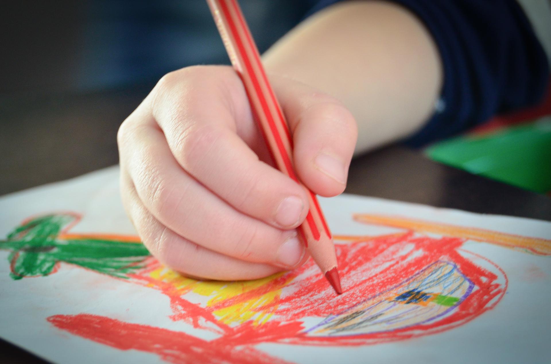 Photograph of a child's hand holding a pencil, doing a colourful drawing