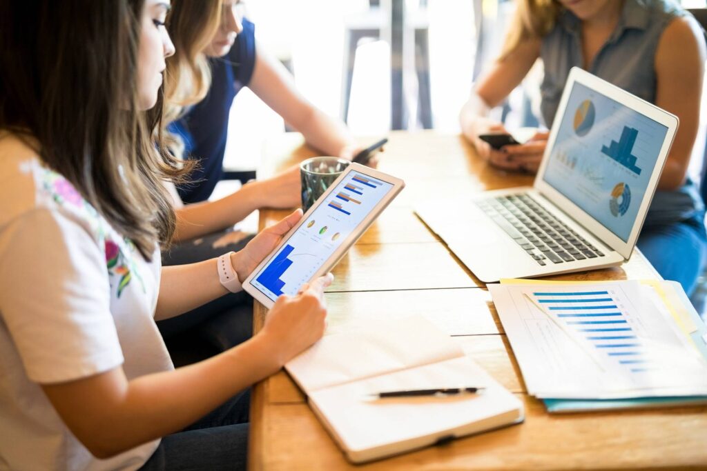 Photograph of a group of people looking at phones, iPads and a laptop around a table